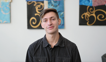 Student Eddie Diaz Serrano shown in black collared shirt in white room with modern art designs in the background.