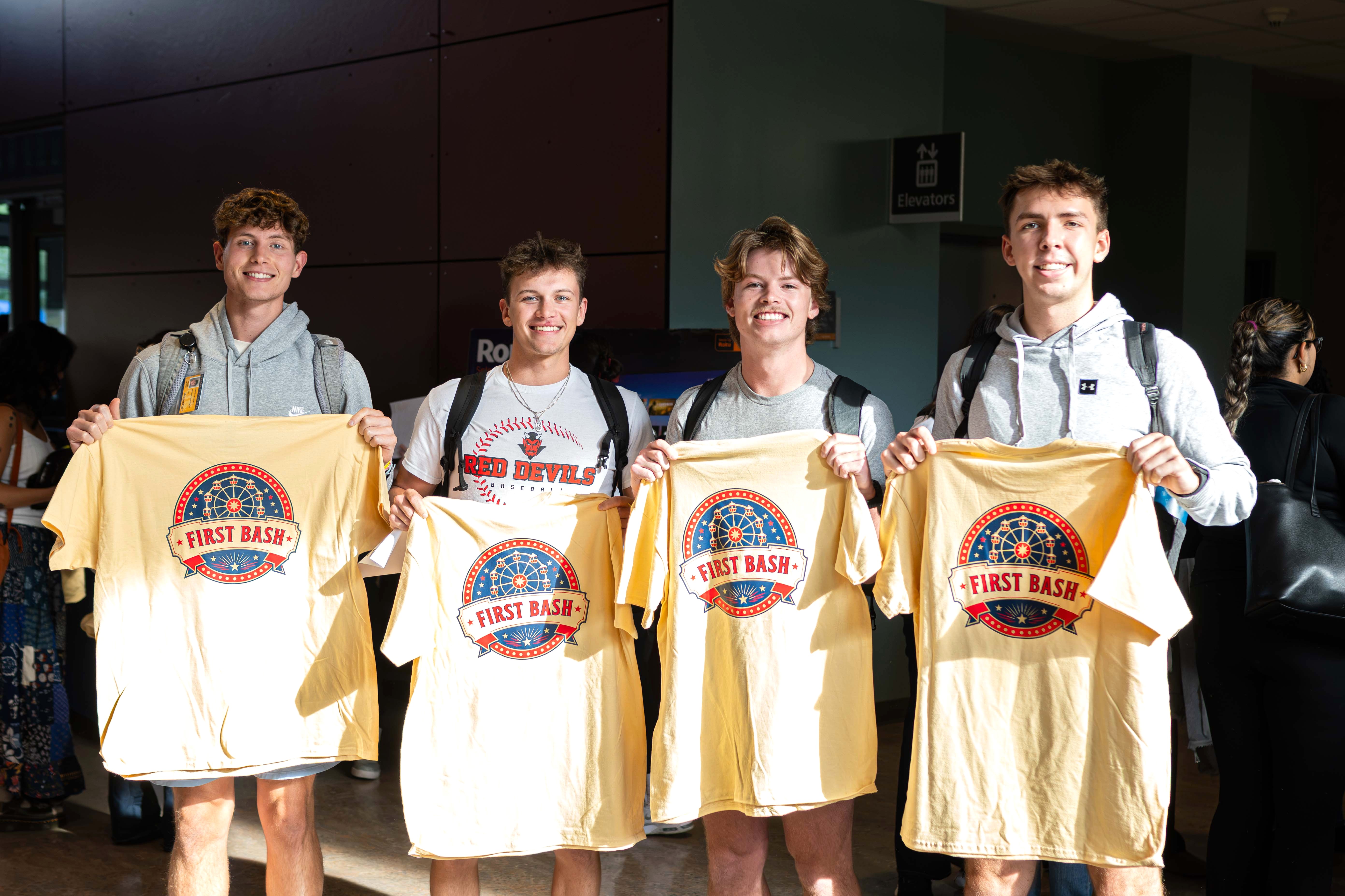 Four students holding First Bash t-shirts