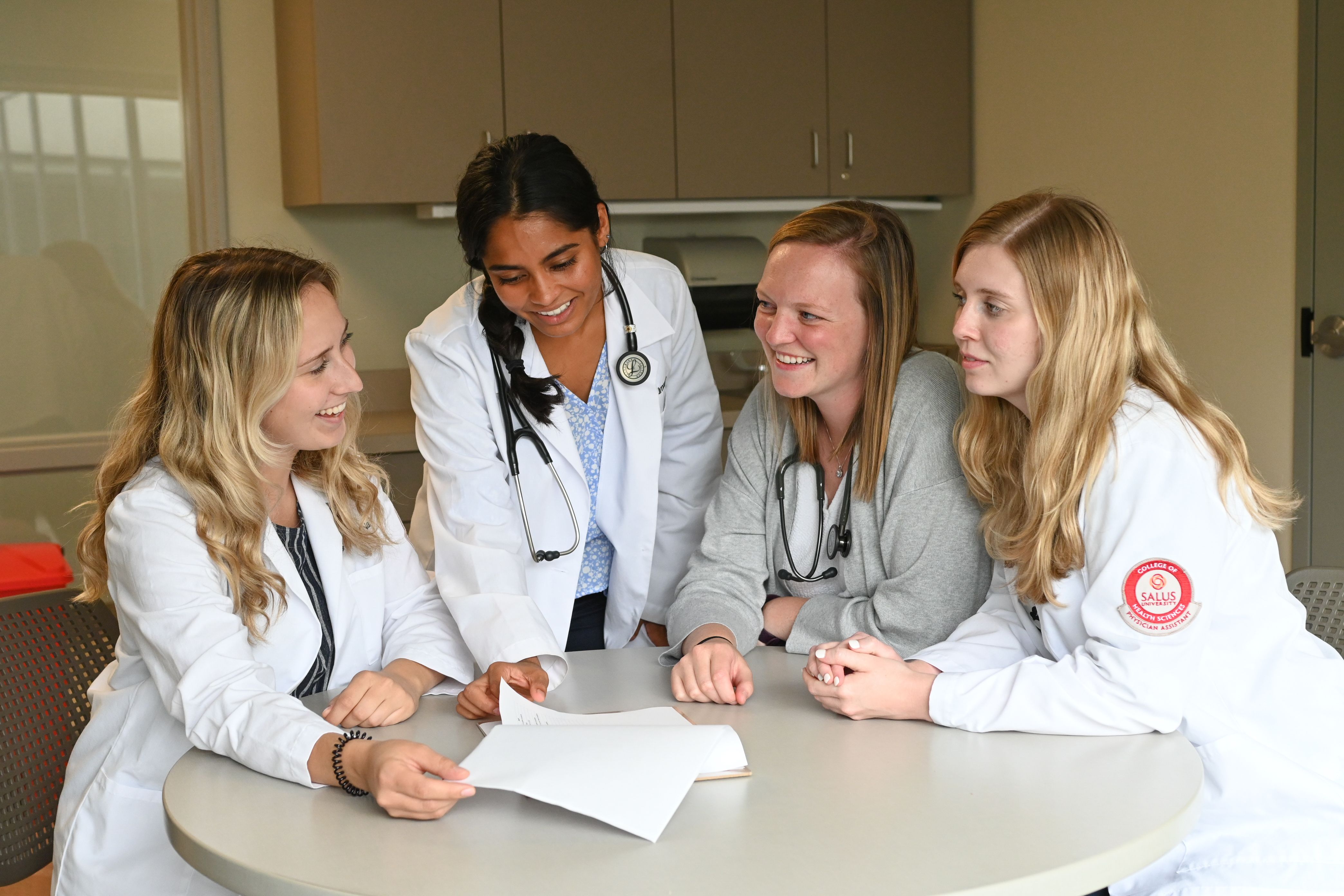 PA students in white coats gathered around a table