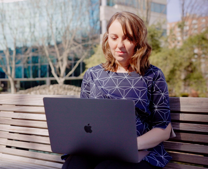 student typing on laptop while sitting on campus bench