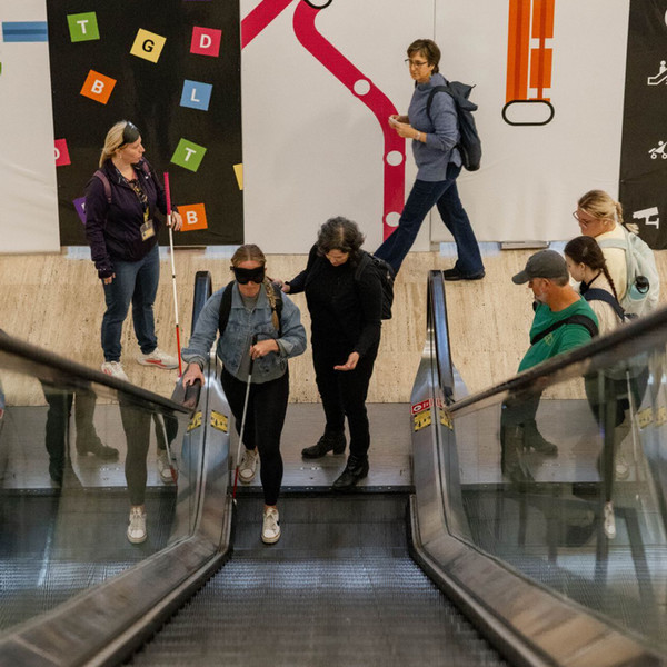 student with white cane navigating escalator with faculty member
