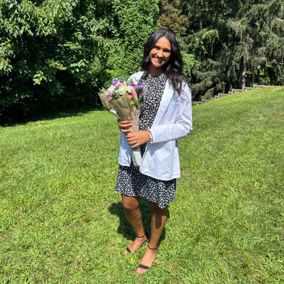 PA student wearing her white coat holding a bouquet of flowers