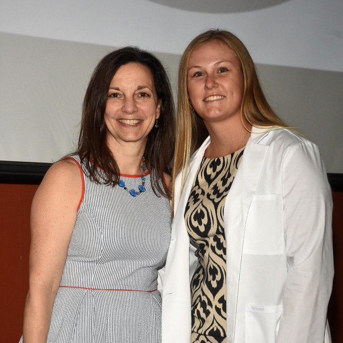 student wearing white coat posing with program director