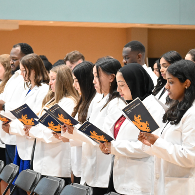 students wearing white coats, reading from program