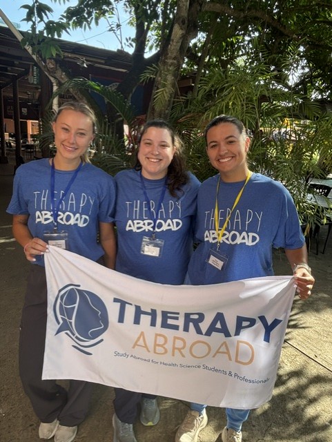 Three Drexel students holding a Therapy Abroad flag