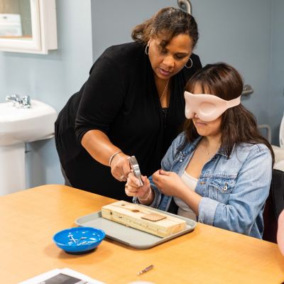 VRT student wearing a blindfold and holding a hammer while being instructed by professor