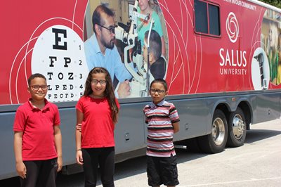 School vision program students standing in front of the big red bus