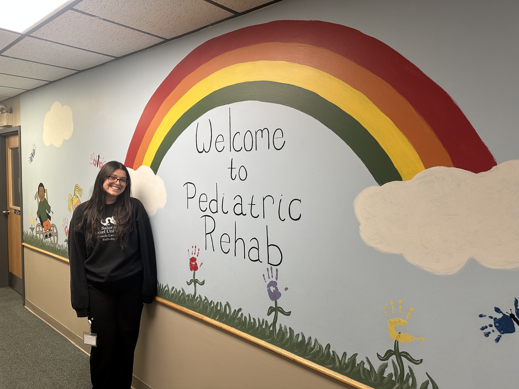 Jenna standing in front of a rainbow painted on a wall