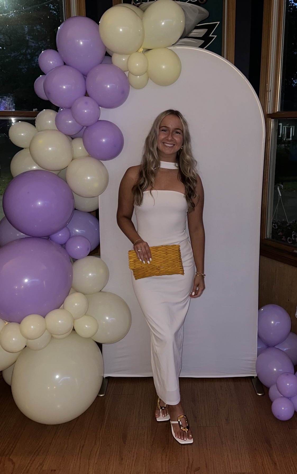 Maddy wearing a white dress in front of a balloon arch