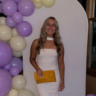 Maddy wearing a white dress in front of a balloon arch