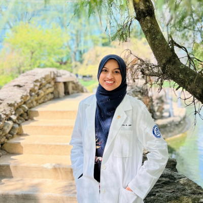 Syeda wearing her white coat in front of the Drexel EPC campus